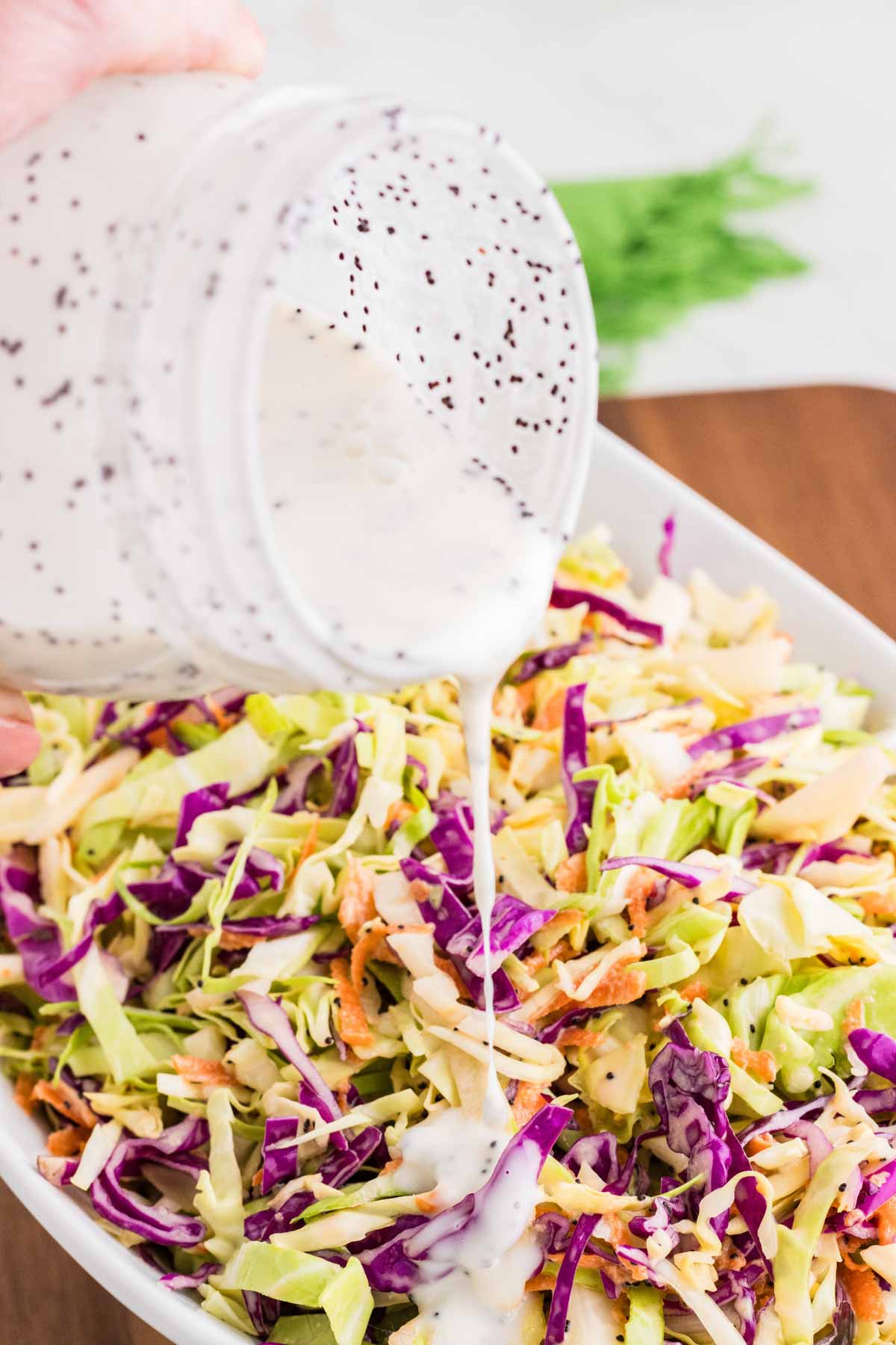 Poppyseed dressing being poured onto coleslaw. 