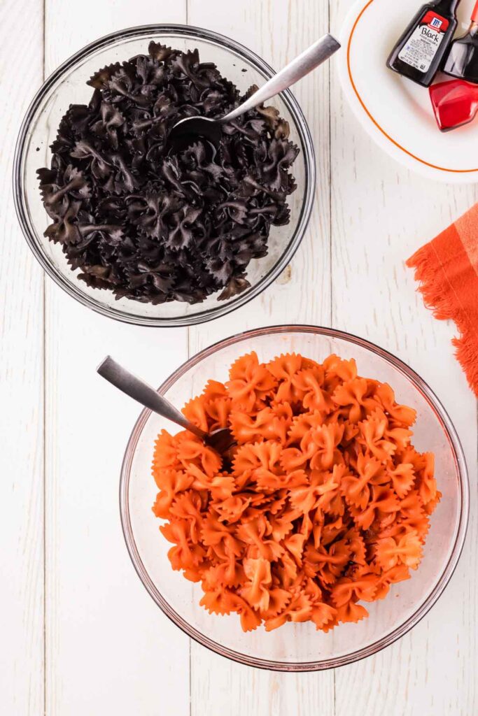 Black and orange dyed pasta in two glass bowls.