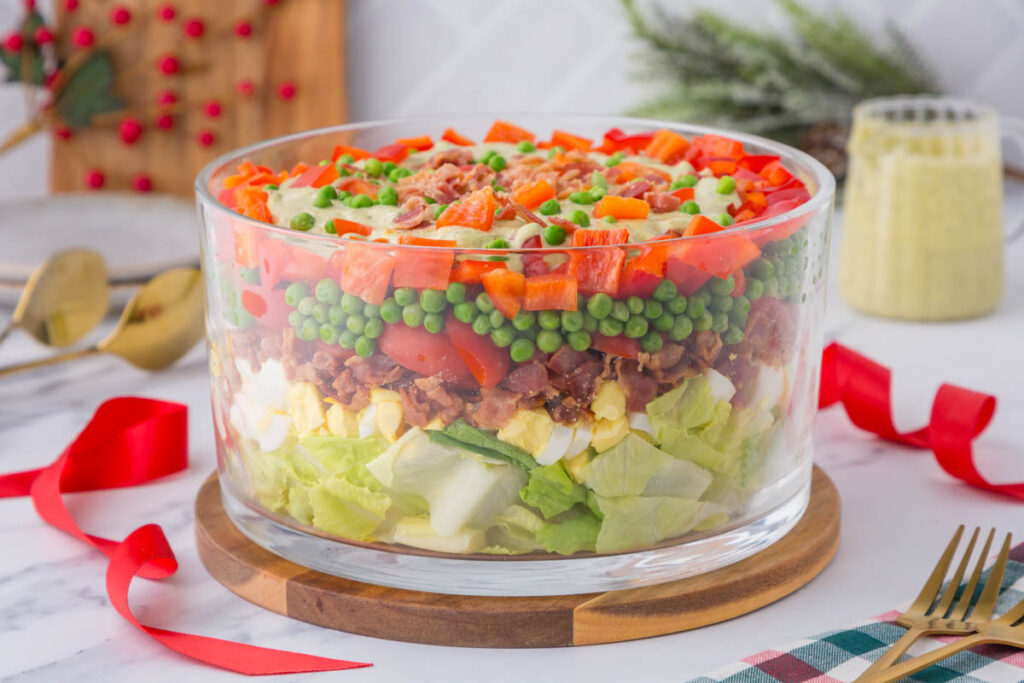 7 Layer Christmas salad in a trifle bowl with pesto ranch.