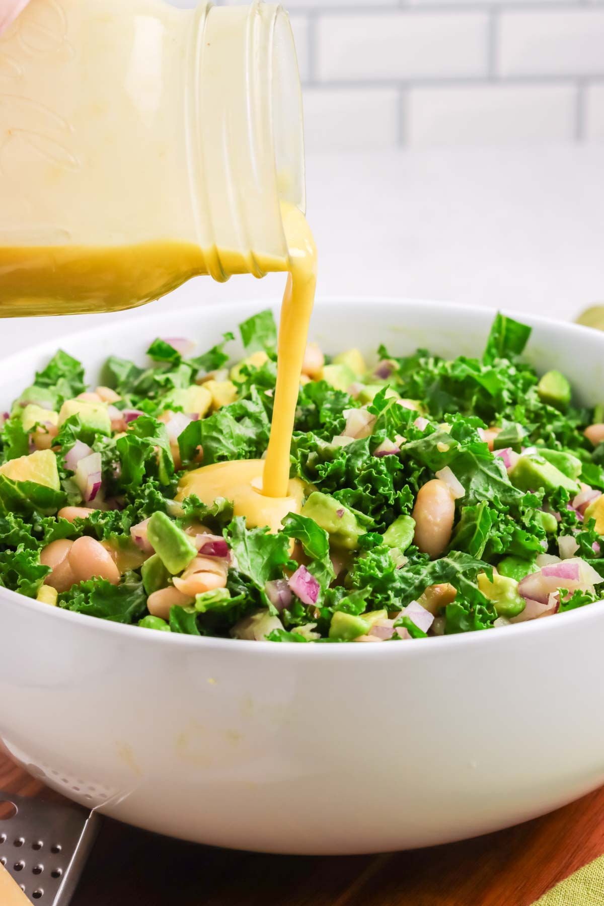 Dijon vinaigrette being poured over a kale salad.