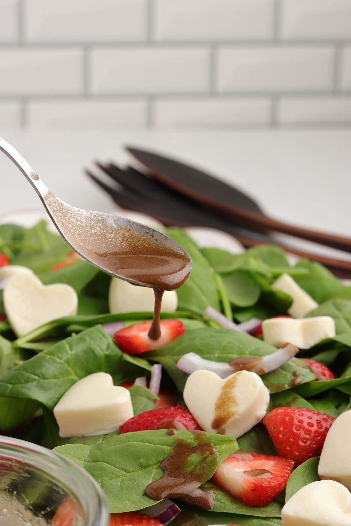 Creamy balsamic dressing being spooned over a spinach salad.
