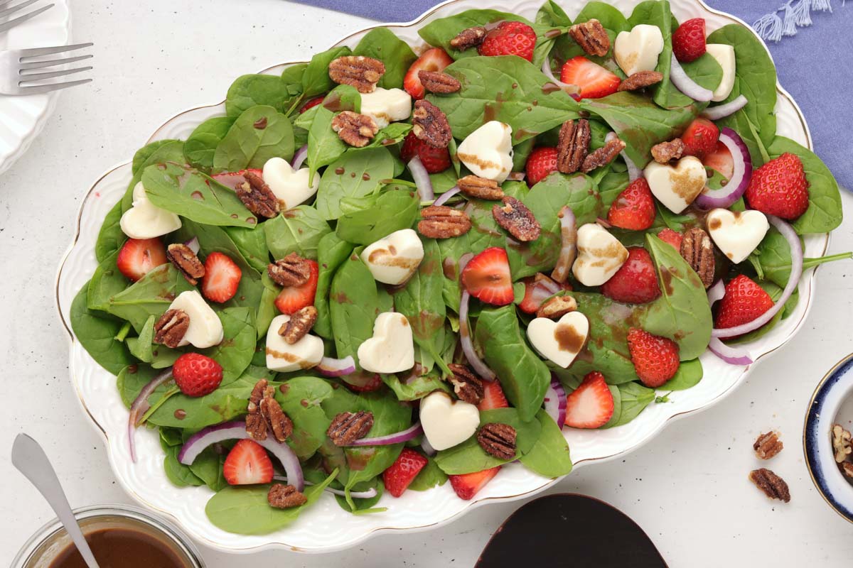A spinach salad which the mozzarella cheese hearts on it.